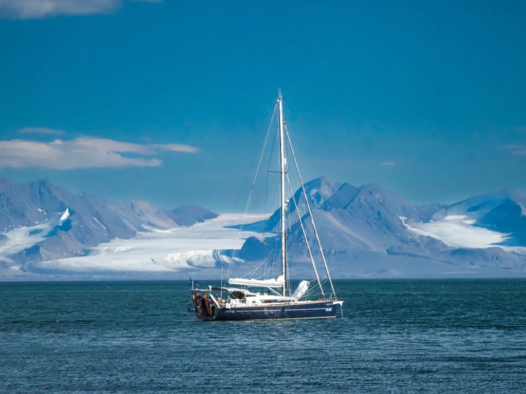 A sailing boat floats on blue water with snow-capped mountains in the background.