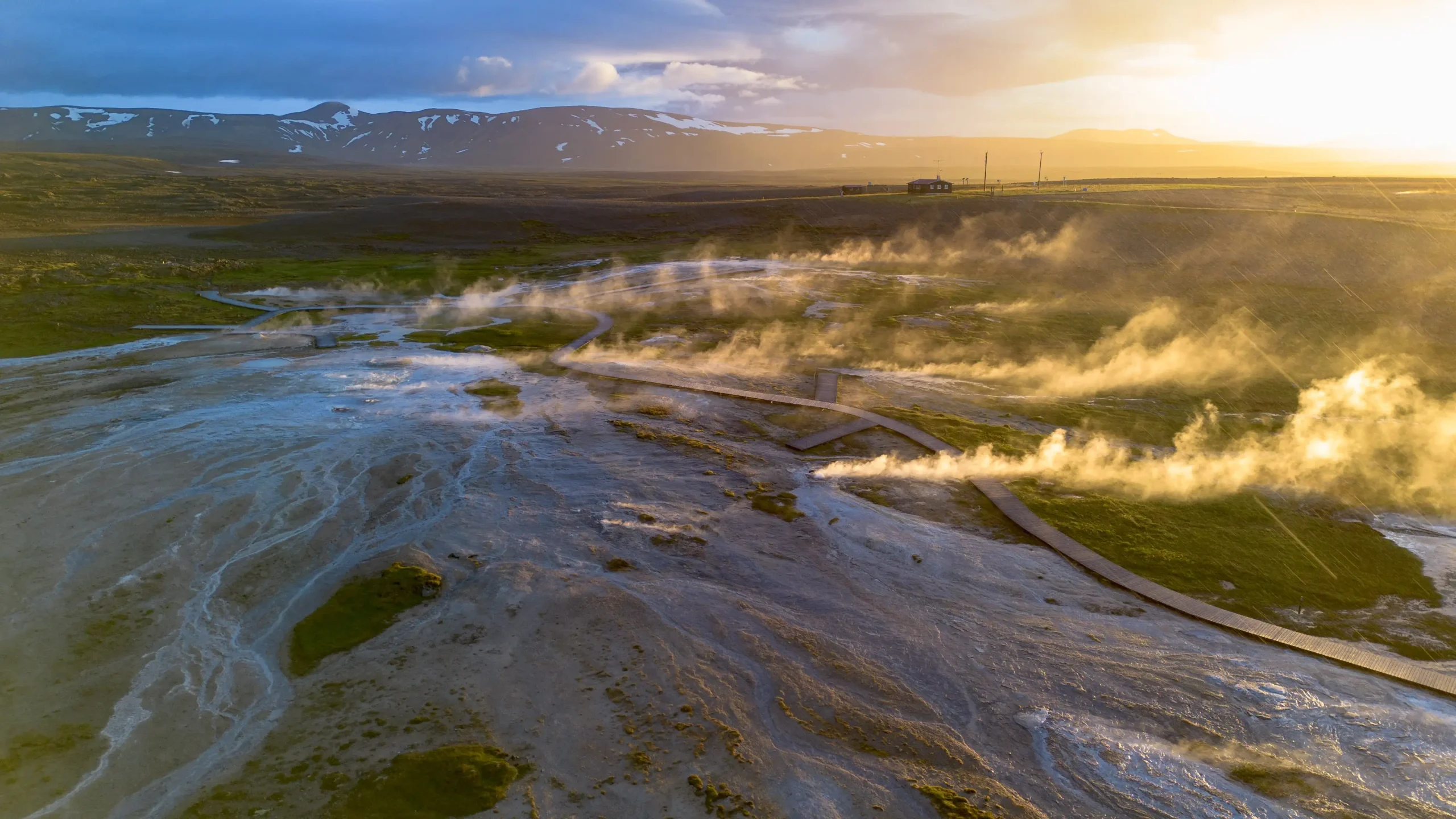 Luftaufnahme der dampfenden heißen Quellen bei Sonnenaufgang, mit den Reviere-Bergen im Hintergrund.