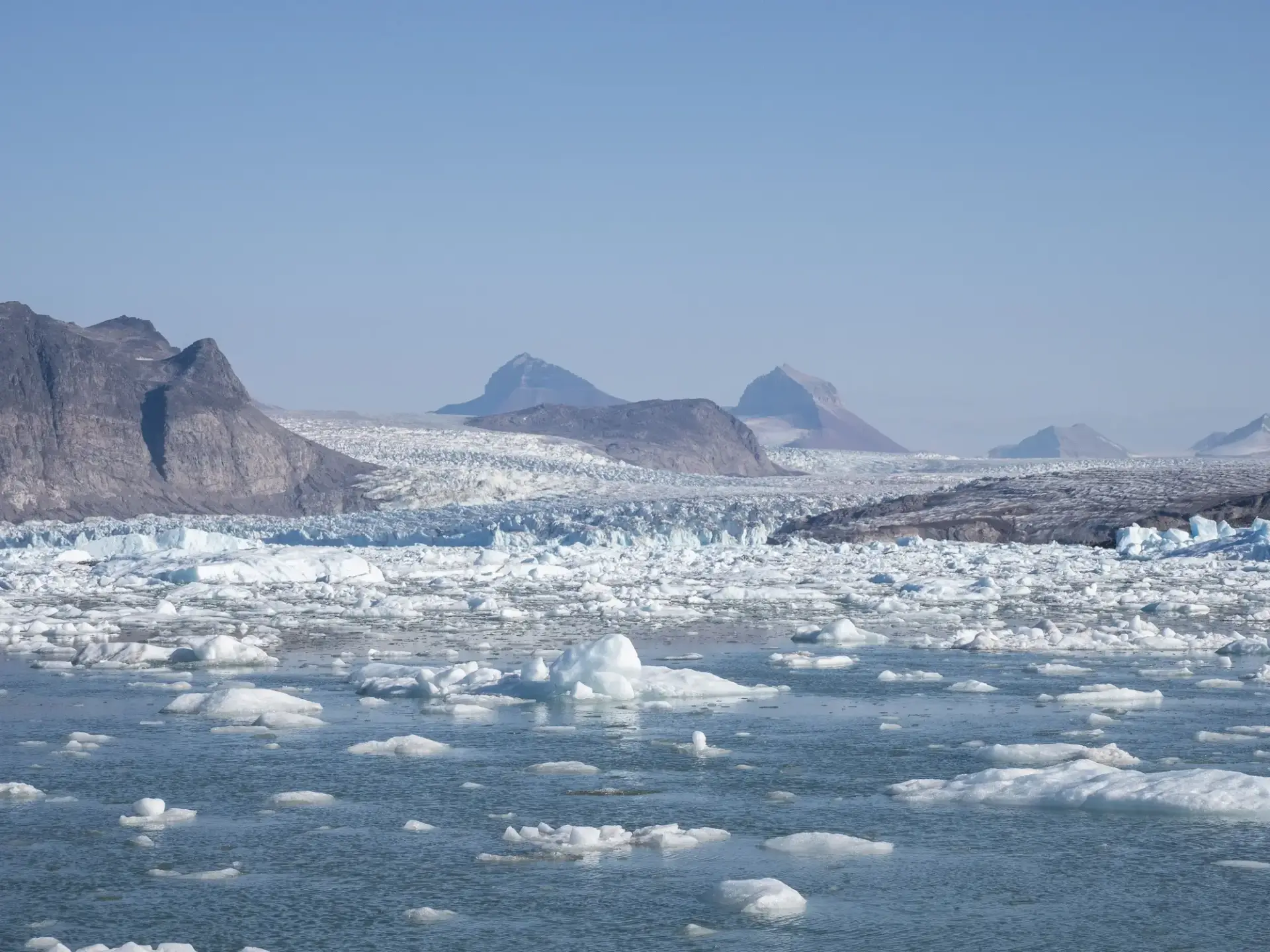 Eisberge treiben in der Nähe von Spitzbergen mit Bergen und einem Gletscher unter einem klaren Himmel.