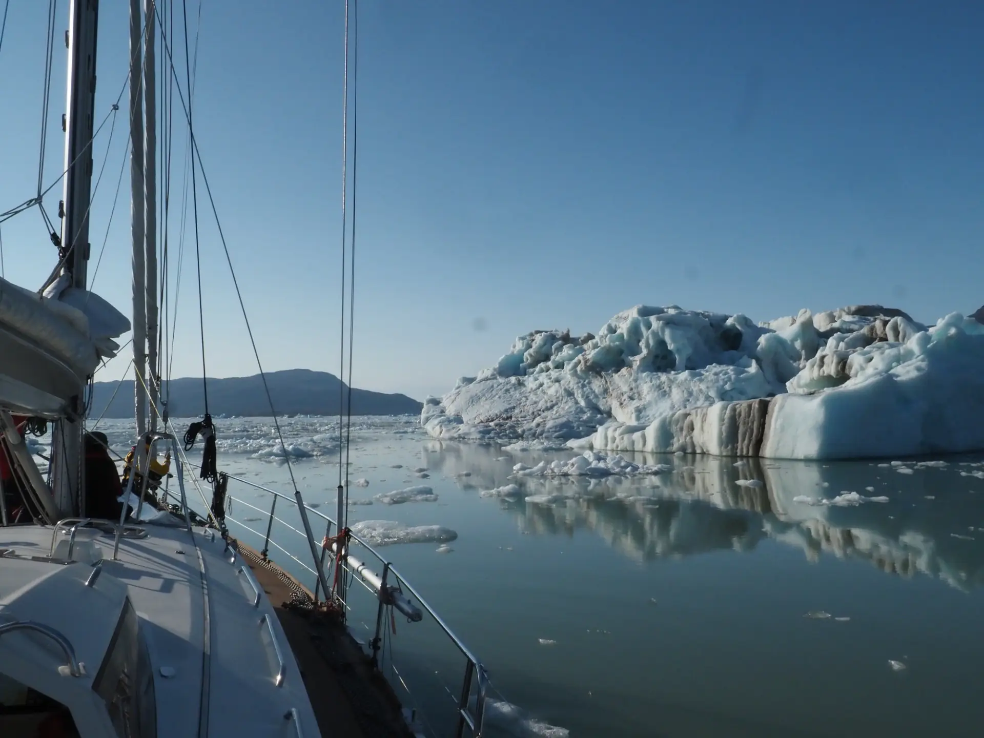 Ein Segelboot nähert sich einem großen Eisberg vor Spitzbergen in ruhigen, eisigen Gewässern bei klarem Himmel.