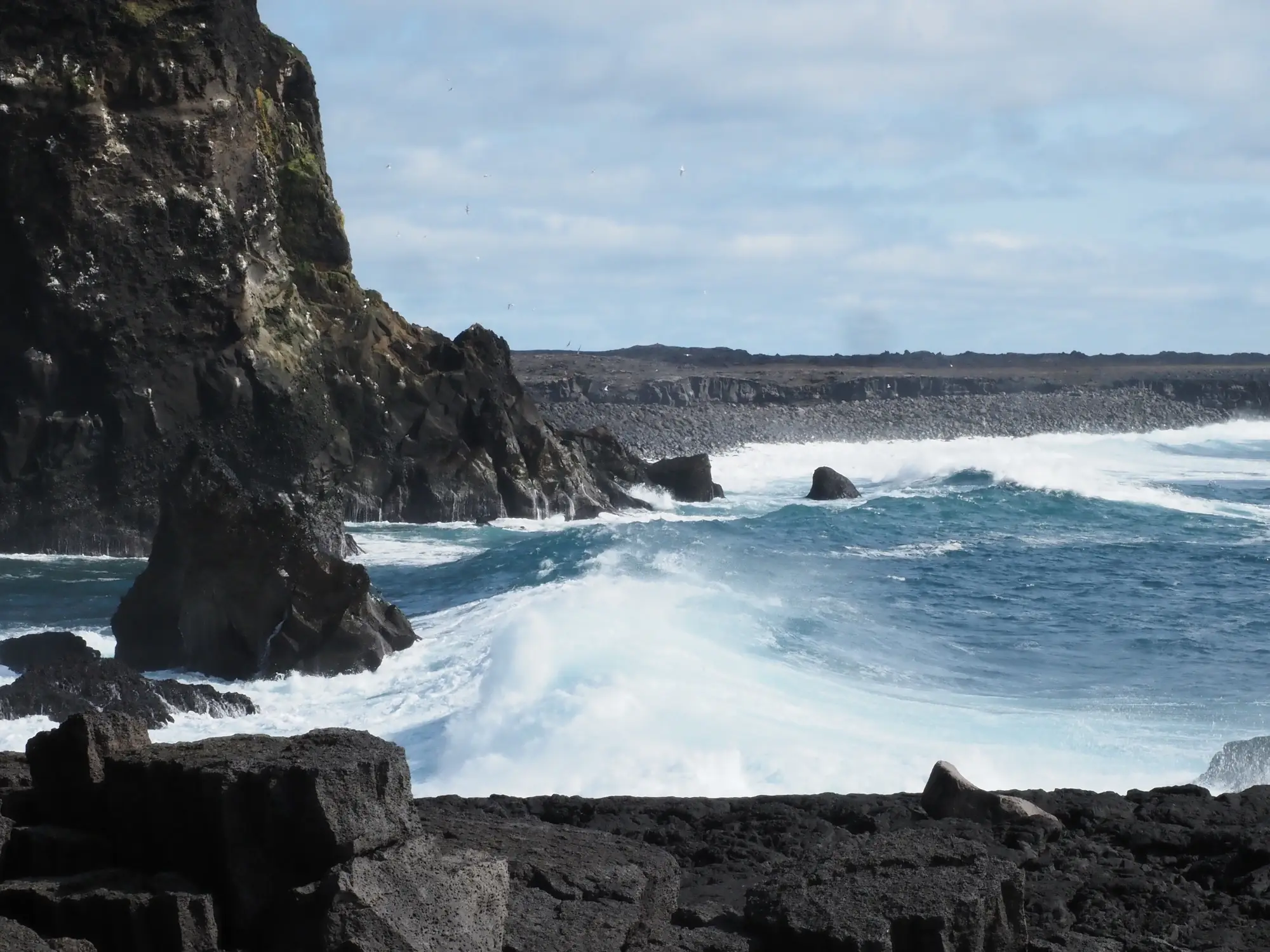 Unter einem teilweise bewölkten Himmel schlagen die Wellen gegen die felsigen Klippen und die Küste der Hebriden.