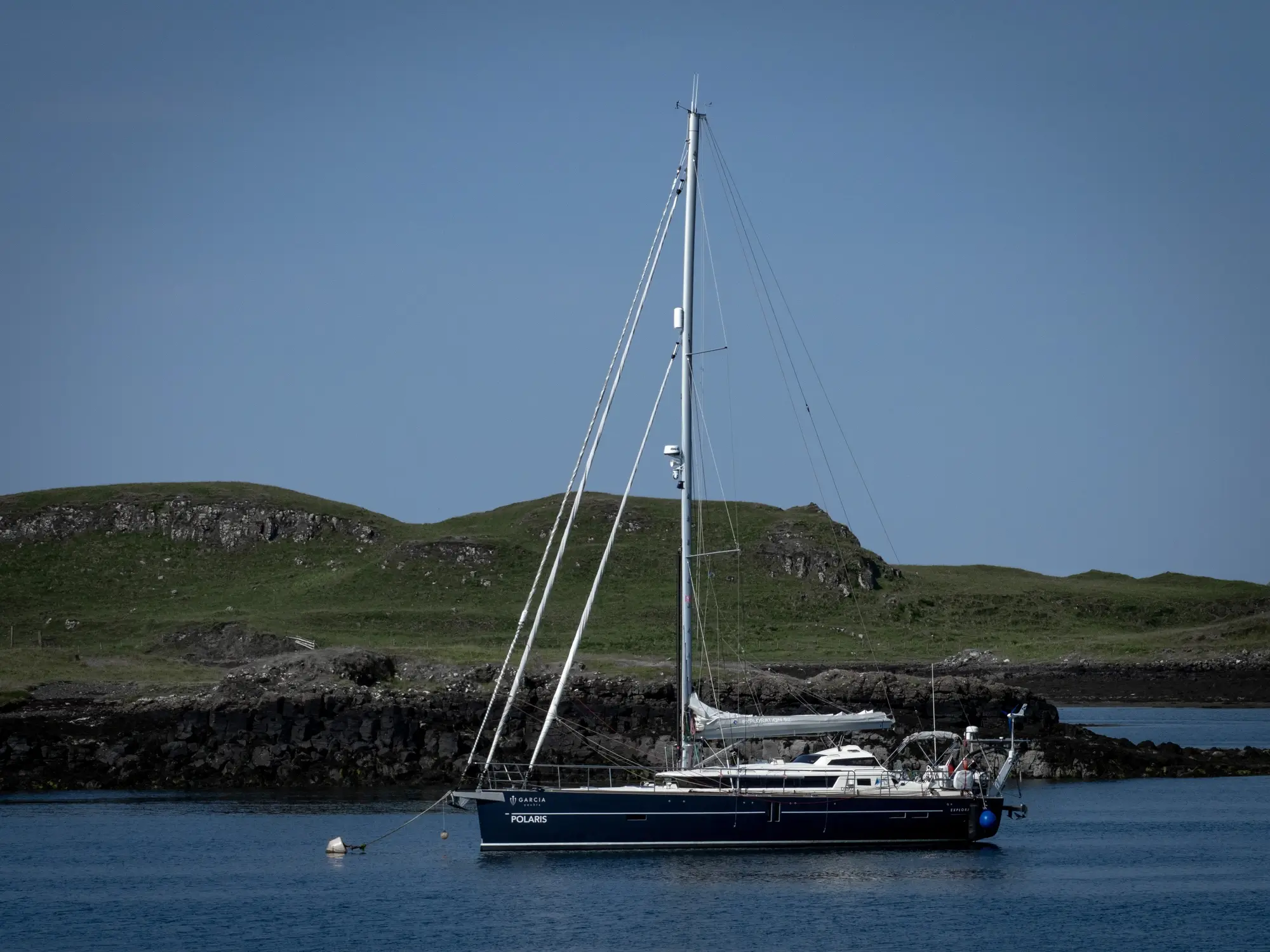 Ein Segelboot ankert in ruhigem Wasser mit den Hebriden-Felsen unter einem klaren Himmel.