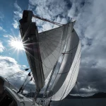 Ein Segelboot mit vollen Segeln gleitet in der Nähe der Hebriden bei strahlendem Sonnenschein und teilweise bewölktem Himmel.