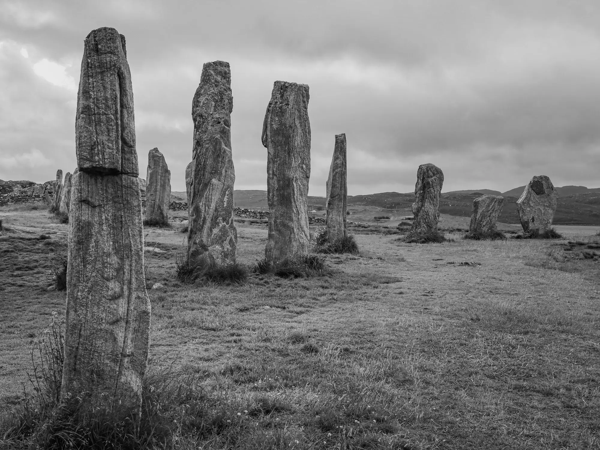 Große stehende Hebridensteine bilden einen Kreis auf einer Wiese unter einem bewölkten Himmel.
