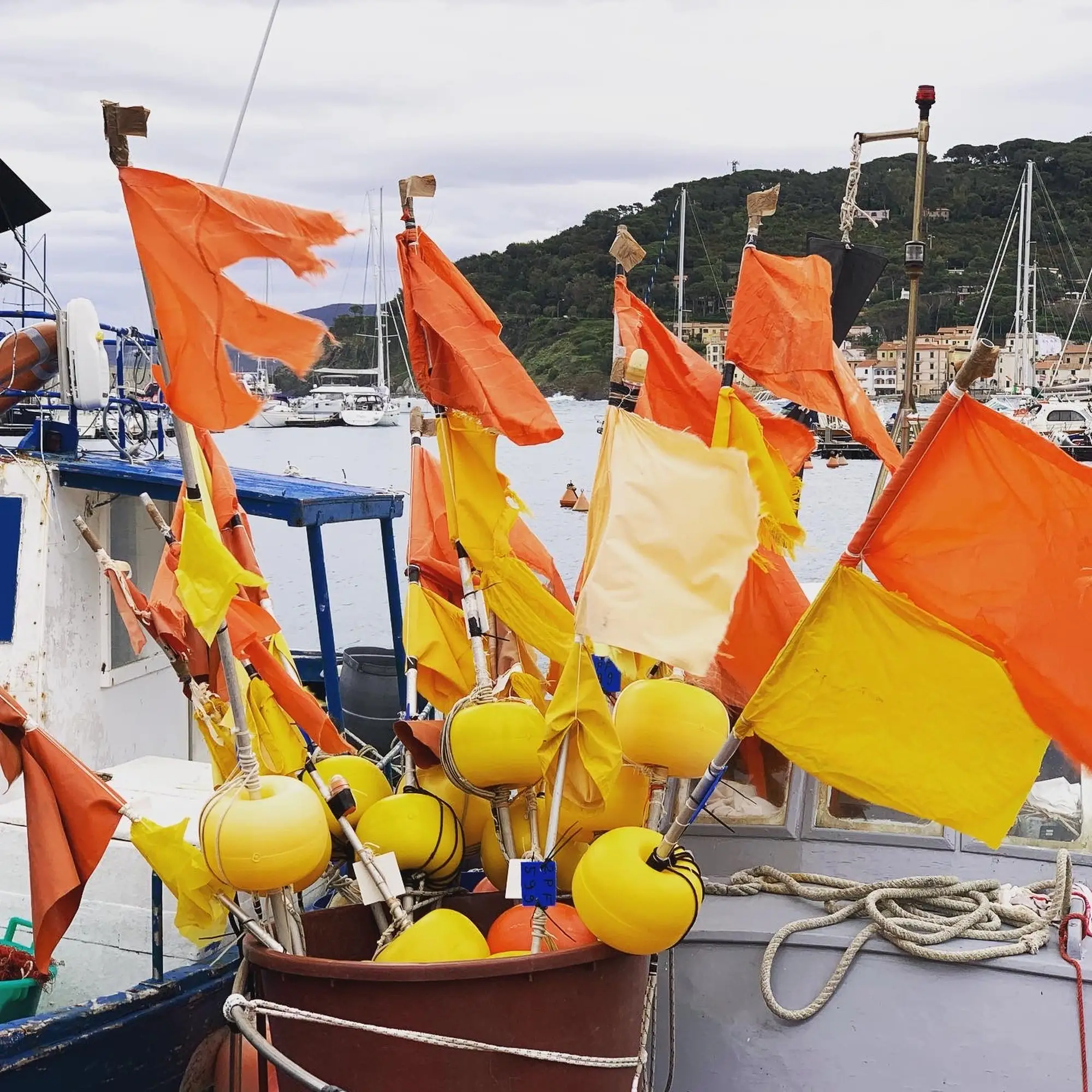 Gelbe und orangefarbene Flaggen und Bojen auf einem angedockten Boot in einem Jachthafen von Kanaren mit Hügeln dahinter.
