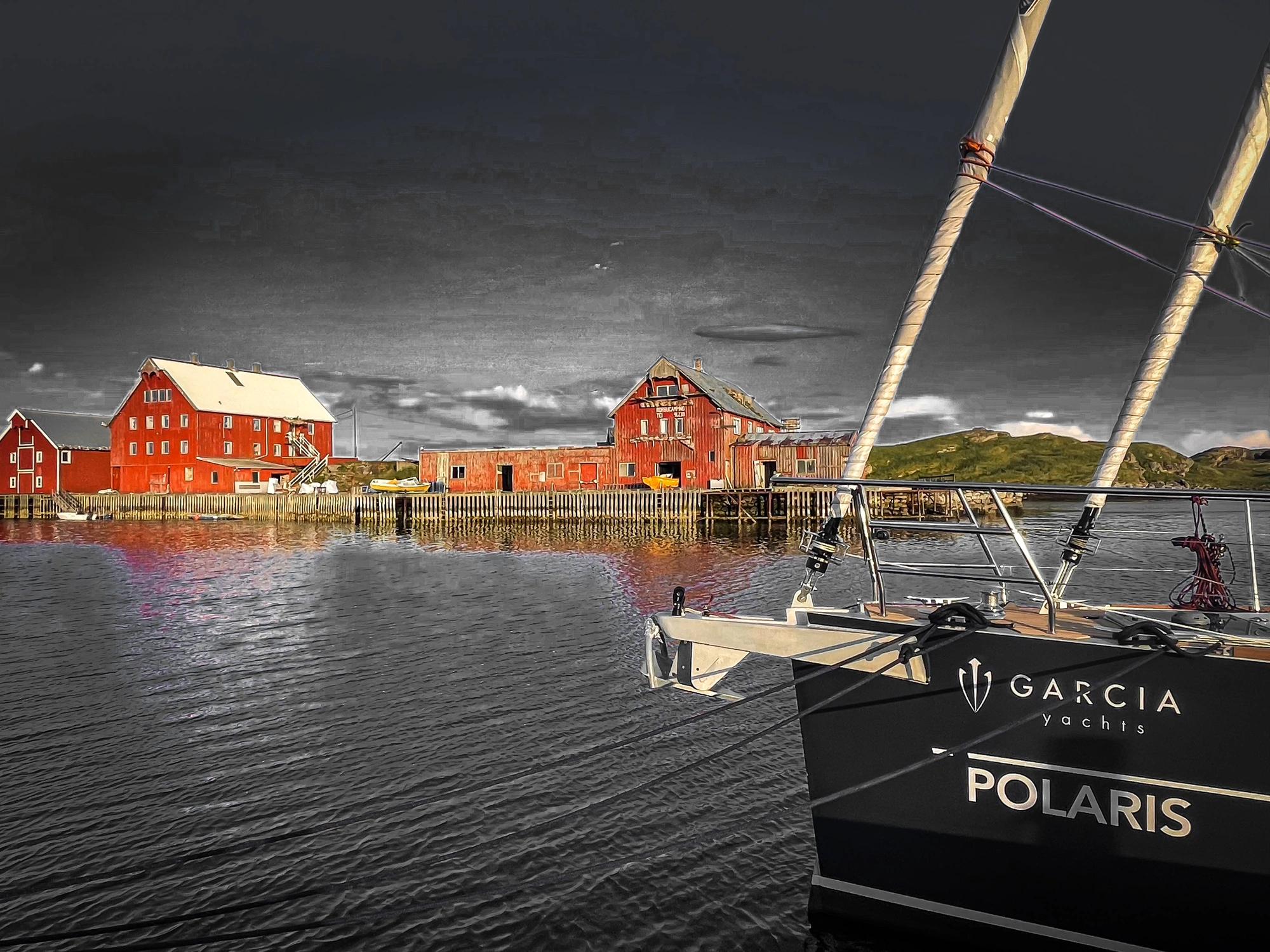 A black yacht named POLARIS on the calm waters of Lofoten near red wooden houses under a cloudy sky.