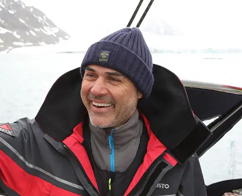 Lächelnder Mann mit blauer Mütze und Winterjacke auf einer Mission in einer verschneiten, eisigen Umgebung.