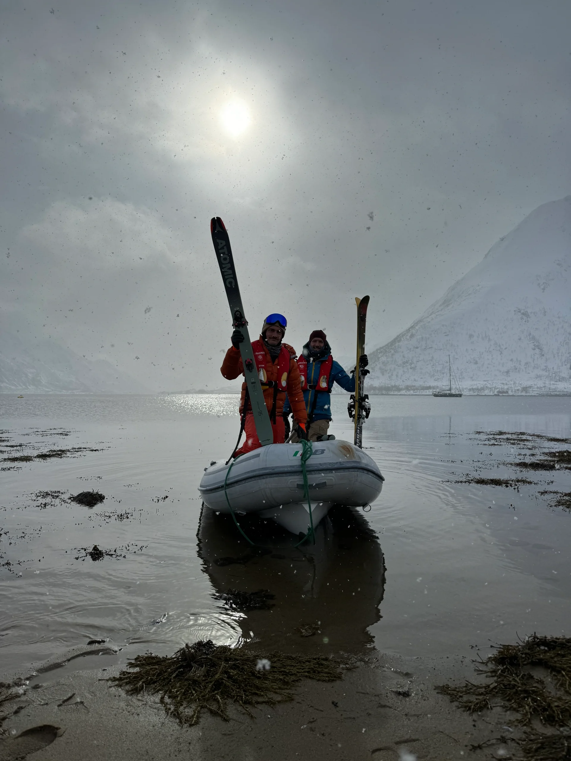 Zwei Skifahrer stehen auf einem Schlauchboot an der verschneiten Küste bei Sail & Ski Lofoten 1 - 270320.