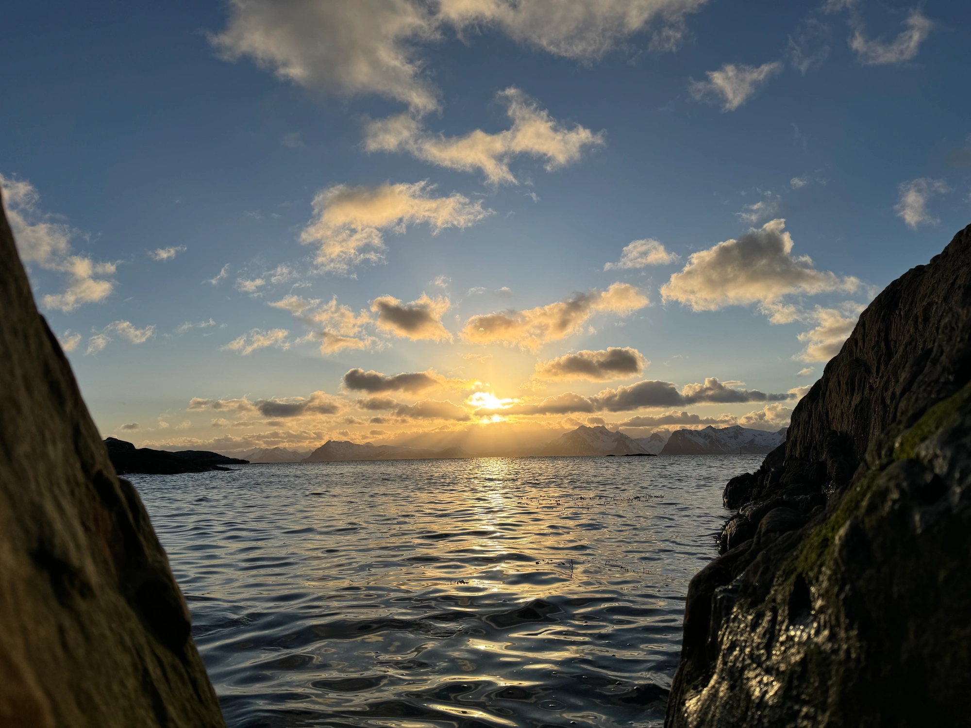 Segeln & Skifahren Lofoten 1 - 270320: Sonnenuntergang über ruhiger See, eingerahmt von Klippen und vereinzelten Wolken darüber.