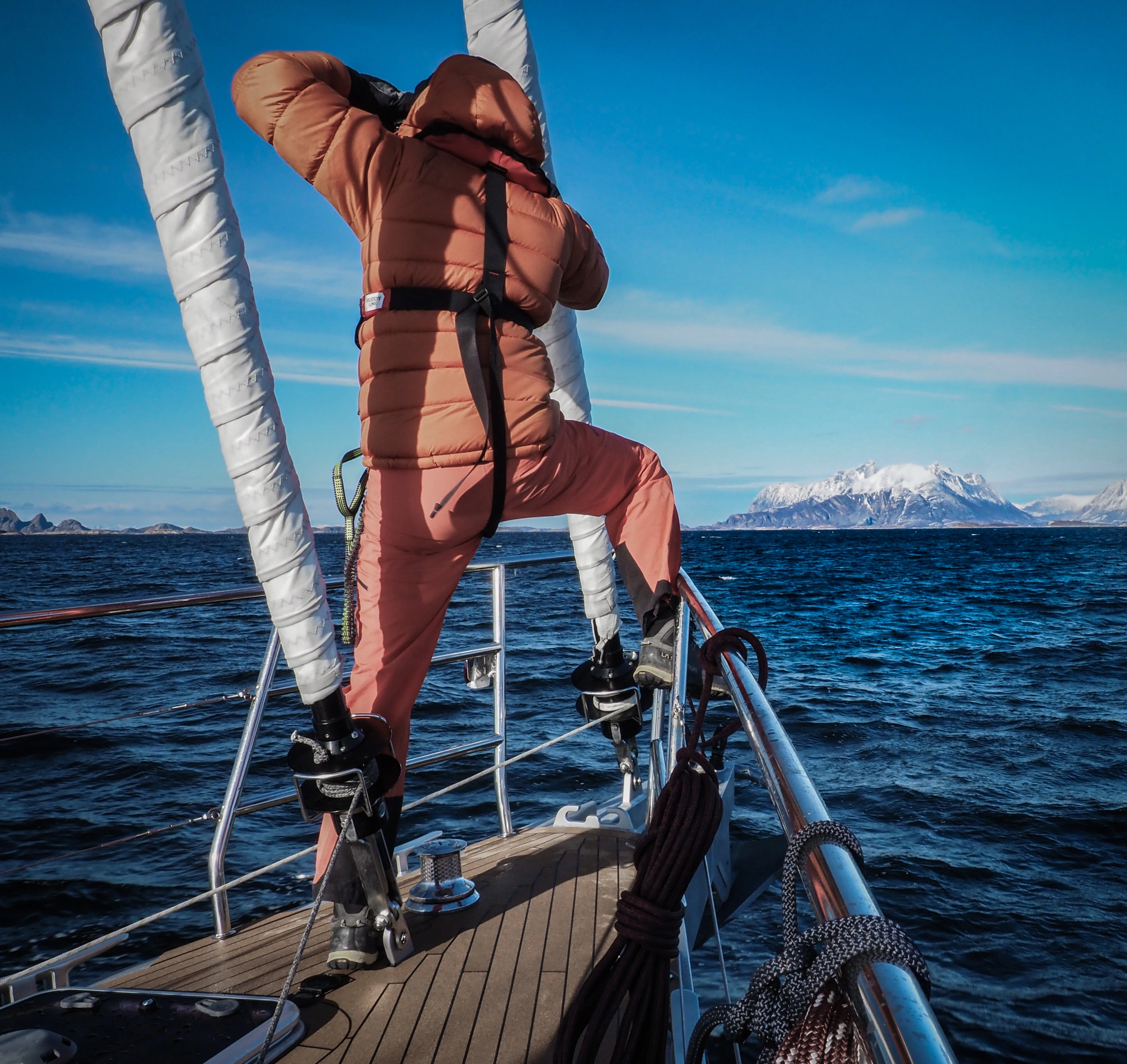 Abenteurer in Orange bewundert die verschneiten Gipfel der Lofoten vom Segelboot Sail & Ski Lofoten 1 - 270320 aus.