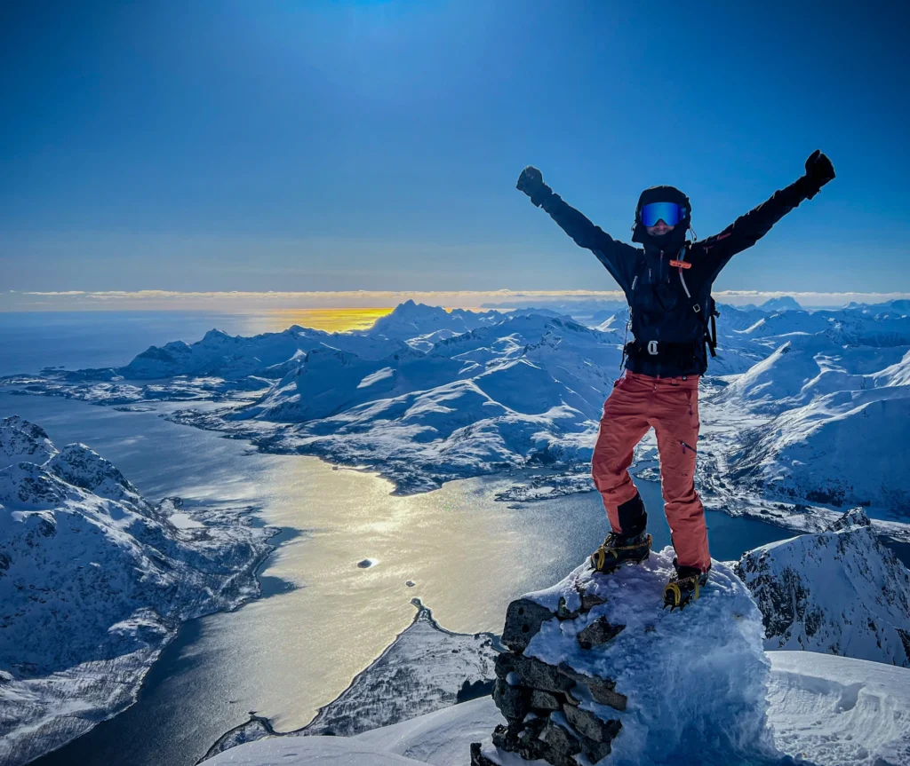 Abenteurer auf dem schneebedeckten Gipfel mit Sail & Ski Lofoten 1 - 270320, mit Blick auf das malerische Meer.