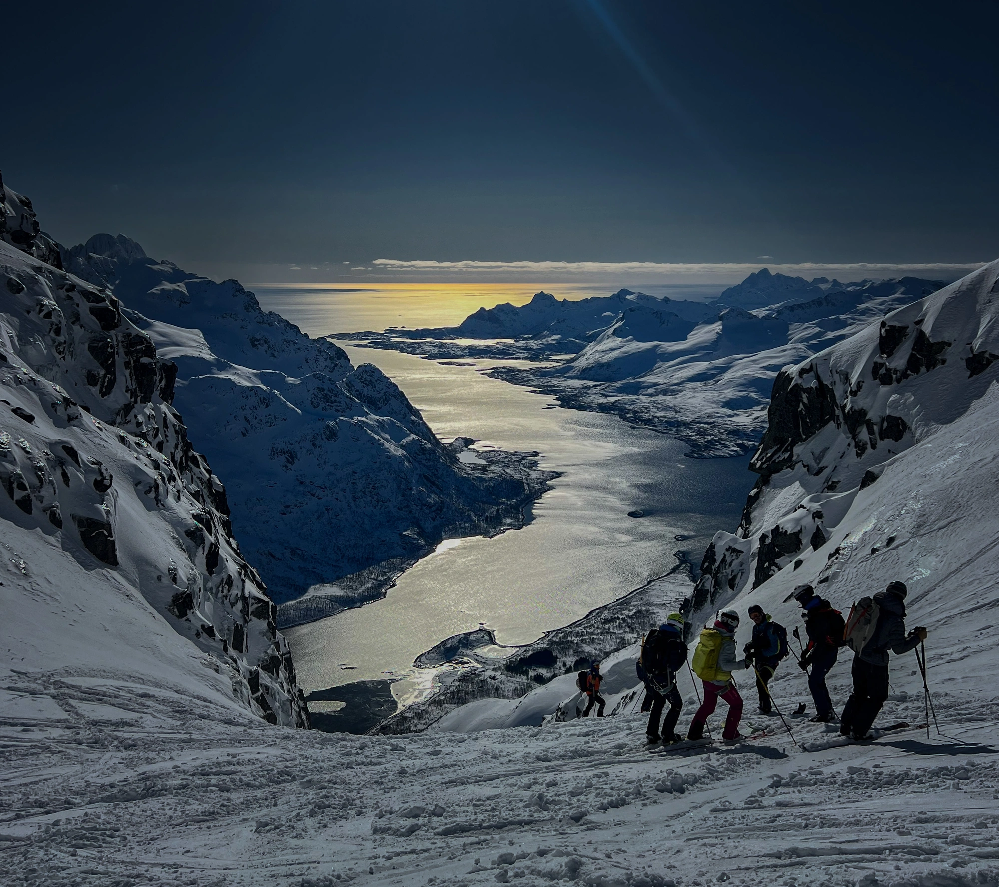 Auf der Sail & Ski Lofoten 1 - 270320 erklimmen Skifahrer verschneite Gipfel mit Blick auf das Meer.